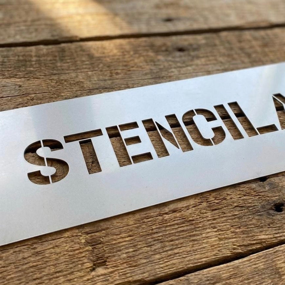 A rectangular white stencil sheet with the word 'STENCILAND' cut out, placed diagonally on a rustic wooden surface.